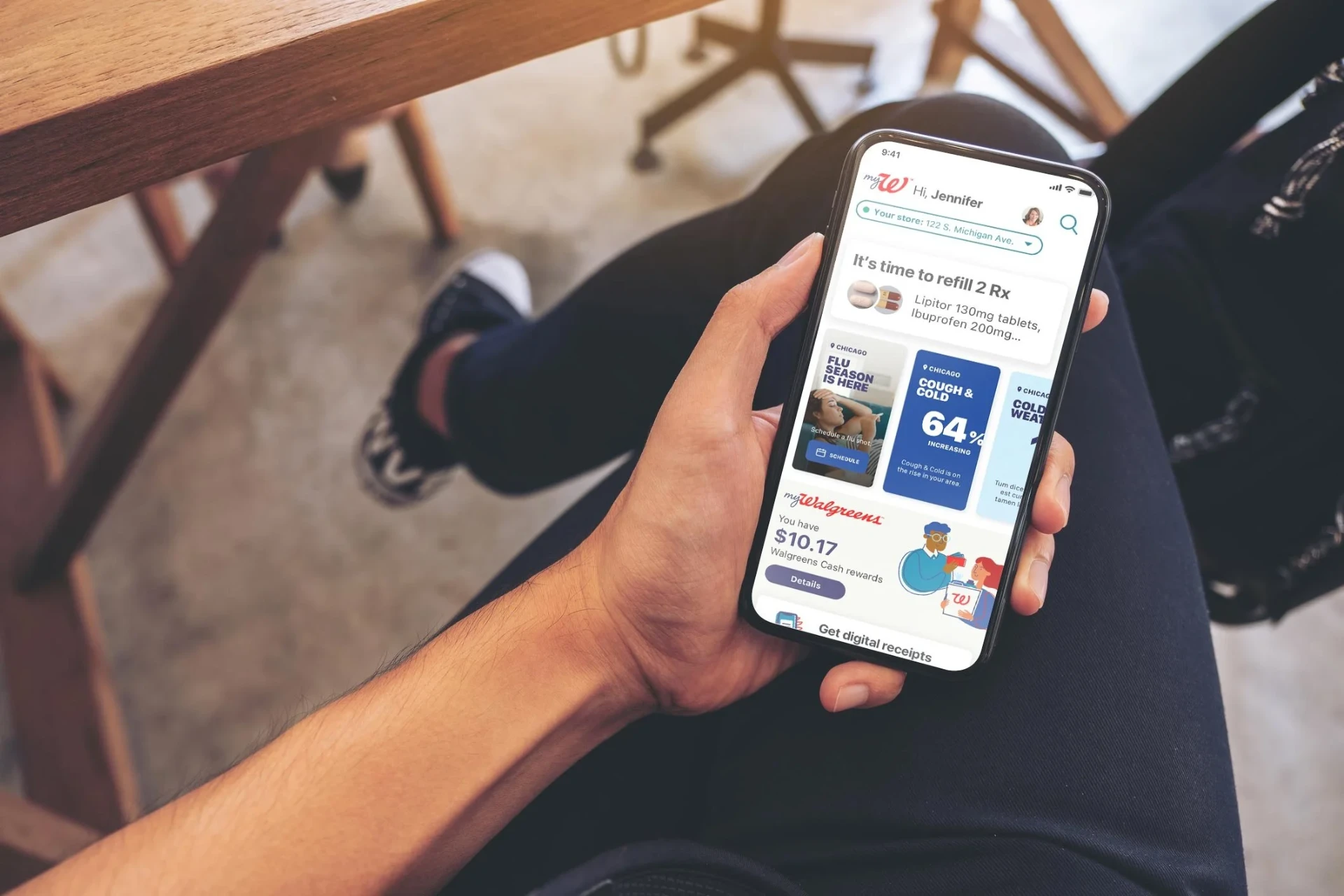 Person holding a phone showing the myWalgreens app home screen with refill, local health alert, and Walgreens Cash rewards cards